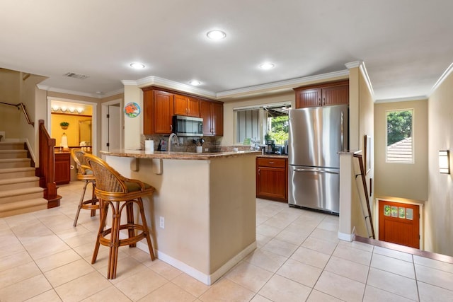 kitchen featuring visible vents, a kitchen breakfast bar, stainless steel appliances, a peninsula, and light stone countertops