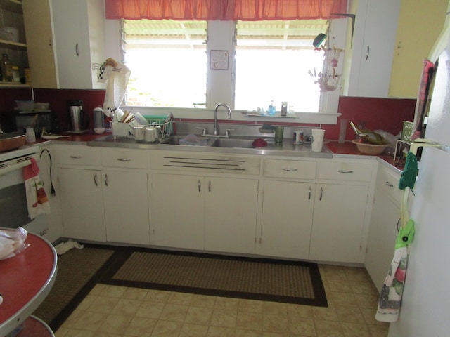 kitchen featuring white appliances, white cabinets, a sink, and light floors