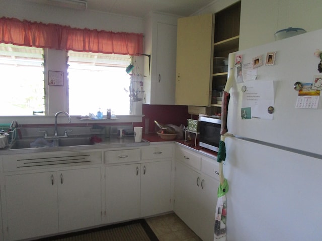 kitchen with light floors, stainless steel microwave, freestanding refrigerator, white cabinetry, and a sink