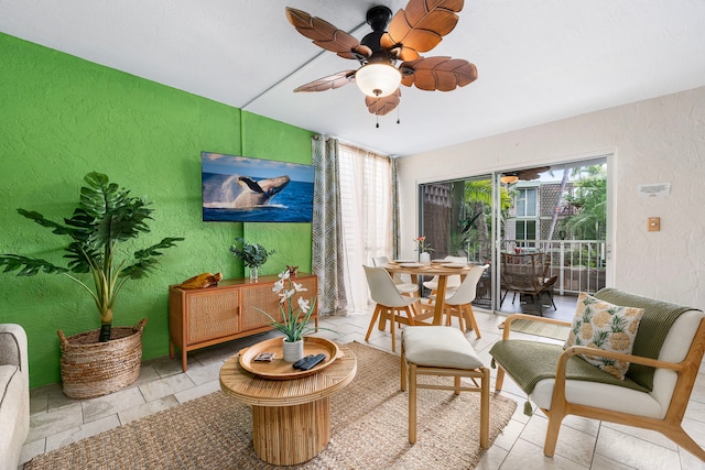 living area with a ceiling fan and a textured wall