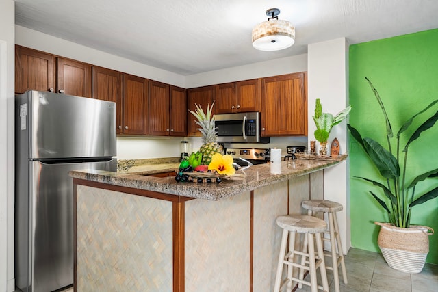 kitchen featuring a breakfast bar, light tile patterned floors, appliances with stainless steel finishes, brown cabinetry, and a peninsula