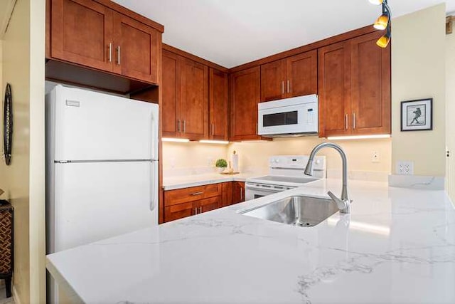 kitchen with light stone counters, brown cabinetry, a sink, white appliances, and a peninsula