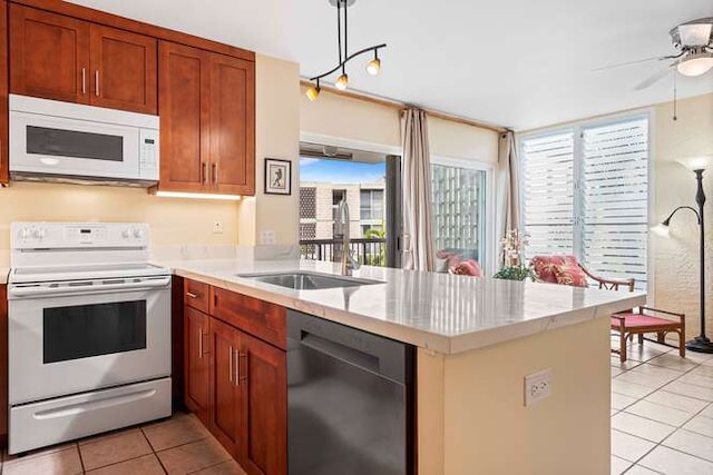 kitchen featuring light countertops, hanging light fixtures, a sink, white appliances, and a peninsula