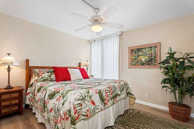 bedroom with a ceiling fan, a textured wall, baseboards, and wood finished floors