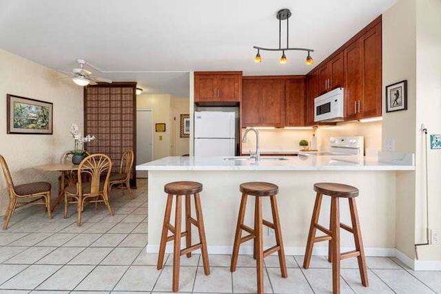 kitchen featuring white appliances, a peninsula, light countertops, pendant lighting, and a sink