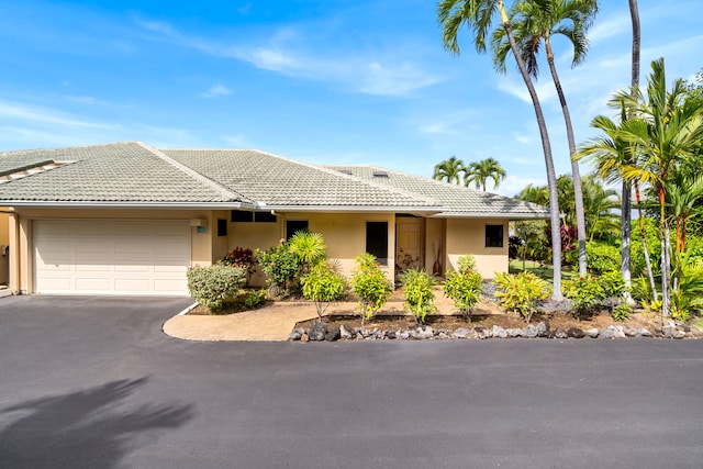 ranch-style house with an attached garage, a tile roof, aphalt driveway, and stucco siding