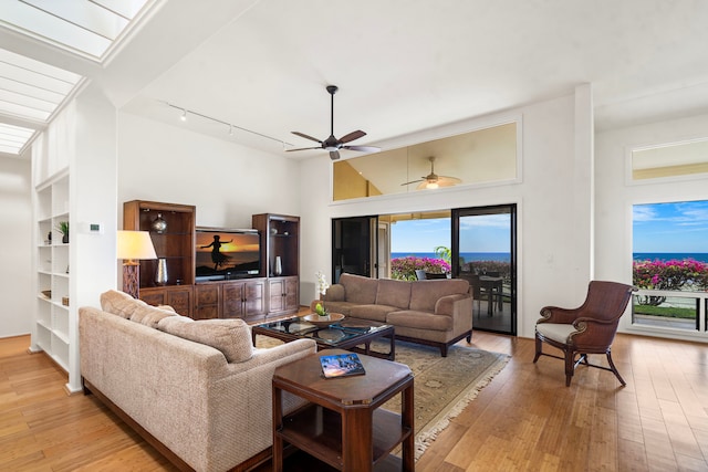 living room featuring light wood finished floors, a skylight, rail lighting, and a ceiling fan