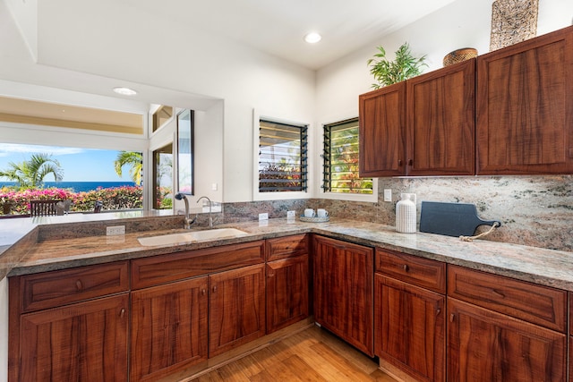 kitchen with brown cabinets, light wood finished floors, tasteful backsplash, a sink, and light stone countertops