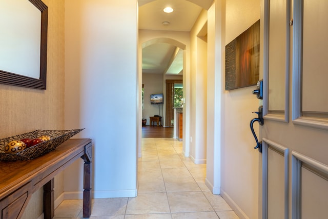 hallway with light tile patterned floors, baseboards, arched walkways, and recessed lighting