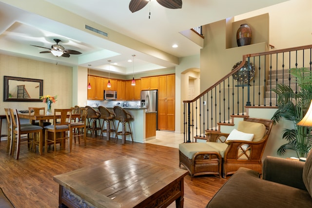 living room featuring arched walkways, light wood-style flooring, visible vents, a ceiling fan, and a tray ceiling