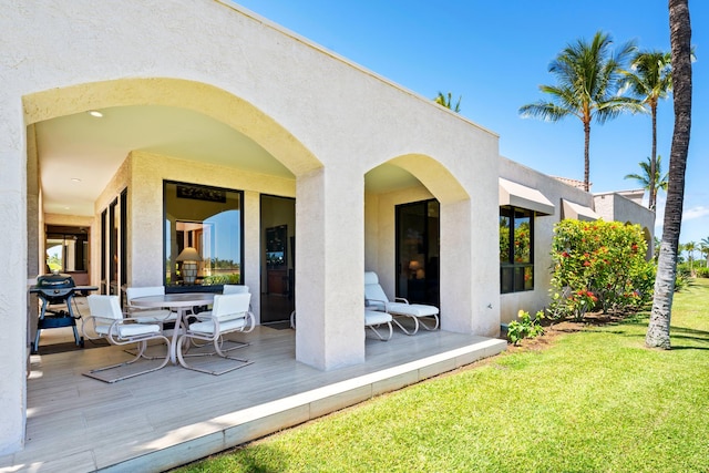 rear view of house featuring outdoor dining area, a yard, and stucco siding