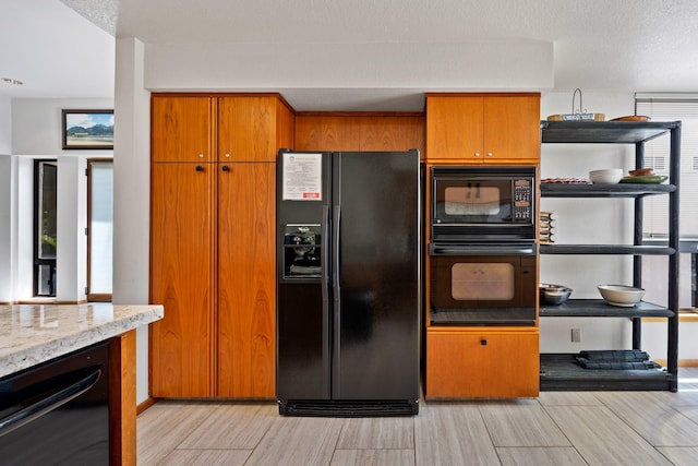 kitchen featuring open shelves, brown cabinetry, a textured ceiling, light stone countertops, and black appliances