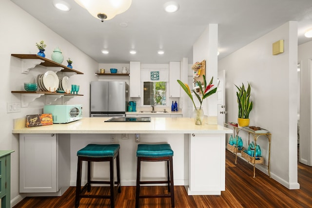 kitchen featuring white microwave, a peninsula, a sink, light countertops, and freestanding refrigerator