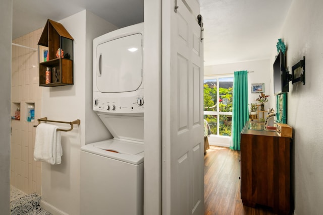 washroom featuring stacked washer and dryer, a barn door, wood finished floors, laundry area, and baseboards