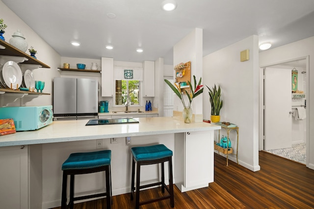 kitchen with a breakfast bar area, open shelves, freestanding refrigerator, white cabinetry, and a sink