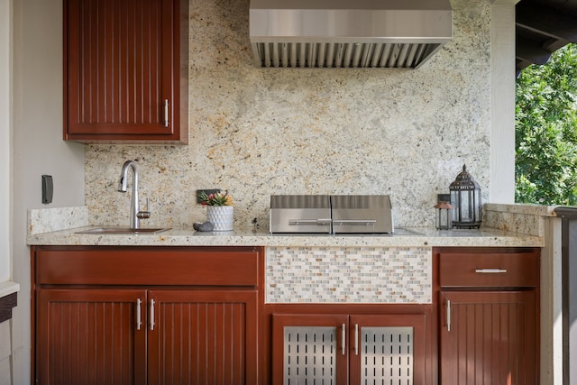 kitchen with light stone counters, range hood, a sink, and decorative backsplash