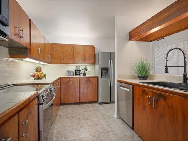 kitchen featuring a sink, tile countertops, appliances with stainless steel finishes, brown cabinetry, and decorative backsplash