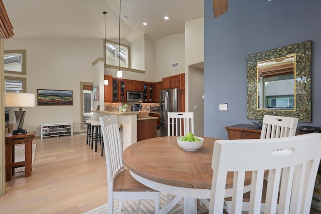 dining space featuring high vaulted ceiling and light hardwood / wood-style flooring