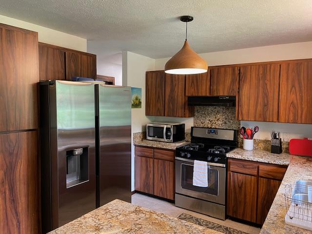 kitchen with stainless steel appliances, decorative light fixtures, light stone counters, light tile patterned floors, and a textured ceiling