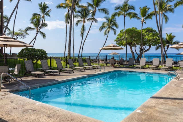 community pool with a water view, a patio area, and fence