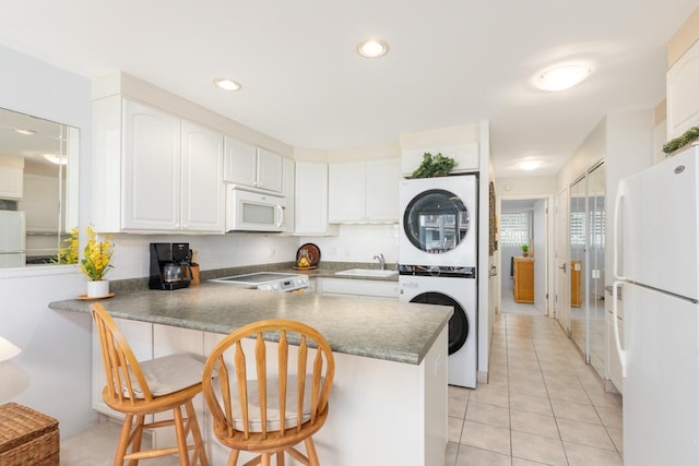 kitchen with a breakfast bar area, stacked washer and dryer, white appliances, a peninsula, and white cabinets