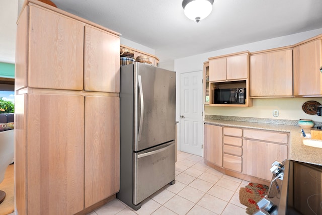 kitchen with black microwave, light brown cabinetry, light tile patterned floors, and freestanding refrigerator