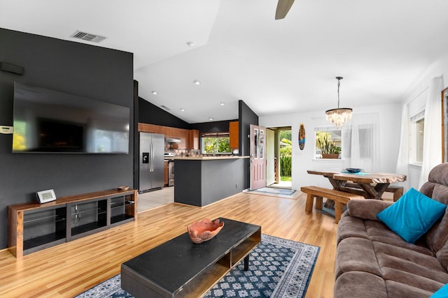 living room featuring a chandelier, light wood-type flooring, visible vents, and vaulted ceiling