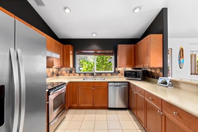 kitchen with under cabinet range hood, a sink, light countertops, appliances with stainless steel finishes, and tasteful backsplash