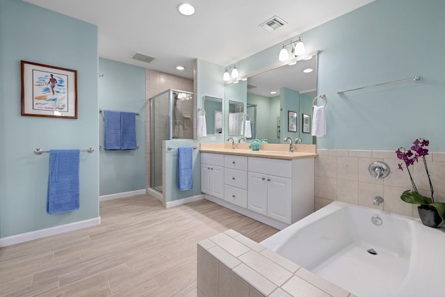 bathroom with a sink, wood finished floors, visible vents, baseboards, and double vanity