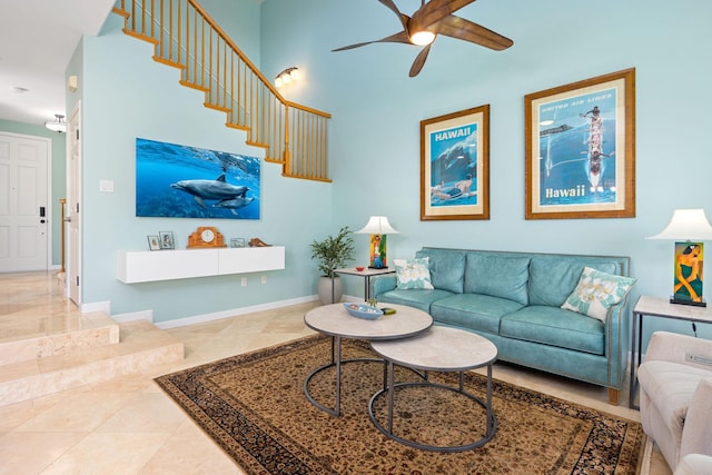 living area with a high ceiling, a ceiling fan, and baseboards