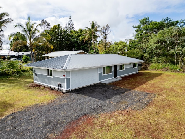 ranch-style home with metal roof, a front yard, gravel driveway, and an attached garage