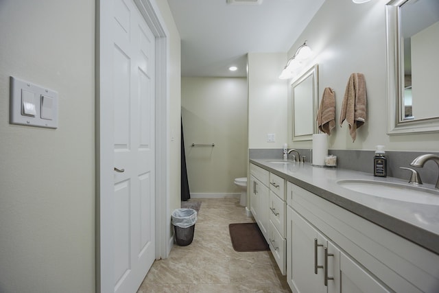 bathroom with double vanity, toilet, baseboards, and a sink