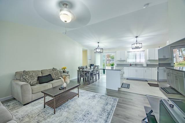 living area featuring an inviting chandelier, light wood-style flooring, baseboards, and vaulted ceiling