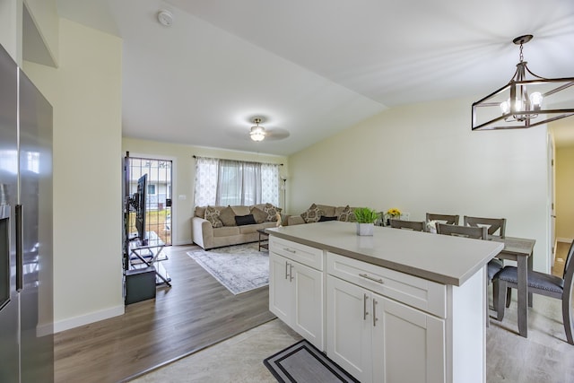 kitchen with decorative light fixtures, vaulted ceiling, light wood-style flooring, stainless steel fridge, and white cabinetry