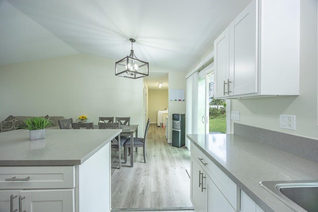 kitchen with light wood finished floors, washing machine and clothes dryer, hanging light fixtures, vaulted ceiling, and white cabinetry