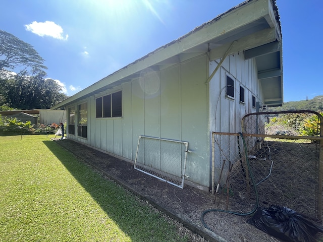 view of property exterior with board and batten siding, fence, and a lawn