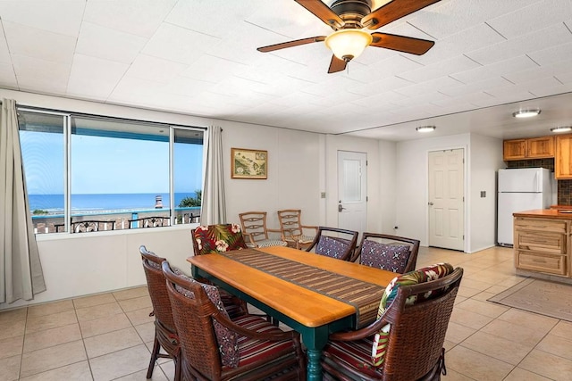 dining space featuring light tile patterned floors, a water view, and a ceiling fan