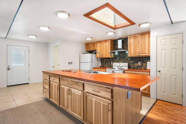 kitchen featuring butcher block counters, white appliances, a skylight, wall chimney exhaust hood, and an island with sink