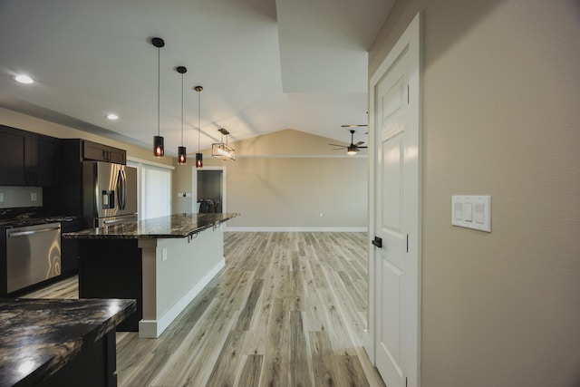 kitchen featuring decorative light fixtures, stainless steel appliances, lofted ceiling, dark stone counters, and light wood-type flooring