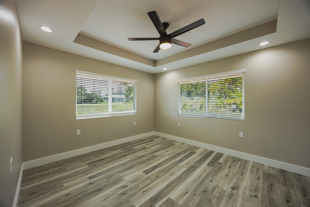 spare room featuring baseboards, a tray ceiling, wood finished floors, and recessed lighting