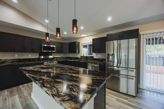 kitchen with light wood-style floors, dark stone counters, and stainless steel appliances