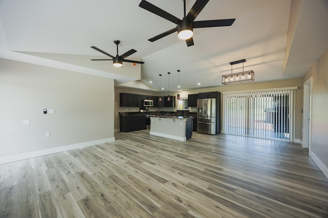 kitchen with open floor plan, appliances with stainless steel finishes, vaulted ceiling, and dark countertops