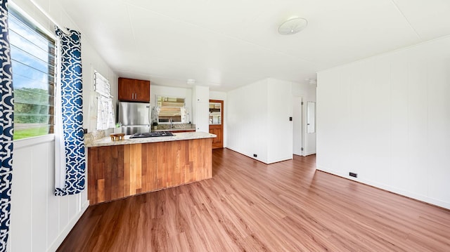 kitchen with brown cabinetry, wood finished floors, a peninsula, stainless steel appliances, and a sink