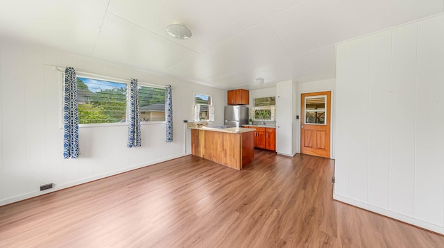 kitchen featuring a peninsula, brown cabinets, wood finished floors, and freestanding refrigerator