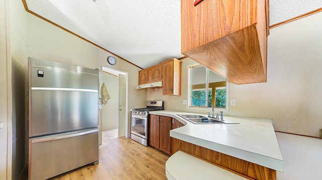 kitchen with under cabinet range hood, a sink, light countertops, stainless steel gas range, and fridge