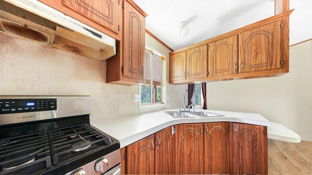 kitchen featuring light countertops, brown cabinetry, stainless steel gas stove, a sink, and under cabinet range hood