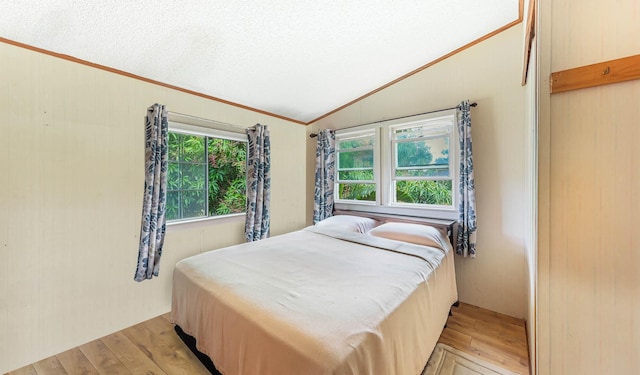 bedroom featuring lofted ceiling, light wood-type flooring, ornamental molding, and a textured ceiling