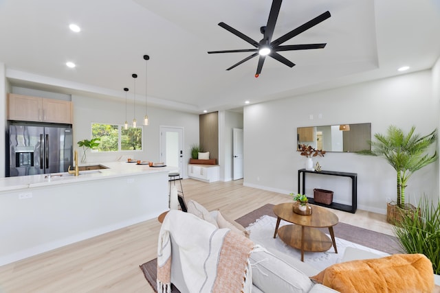 living area featuring light wood-style flooring, recessed lighting, a ceiling fan, baseboards, and a tray ceiling