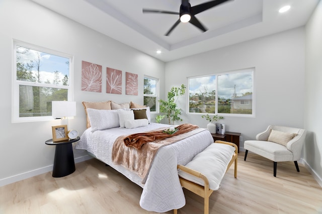 bedroom with a tray ceiling, light wood-style flooring, and baseboards