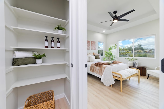 bedroom with light wood finished floors, a raised ceiling, and a ceiling fan